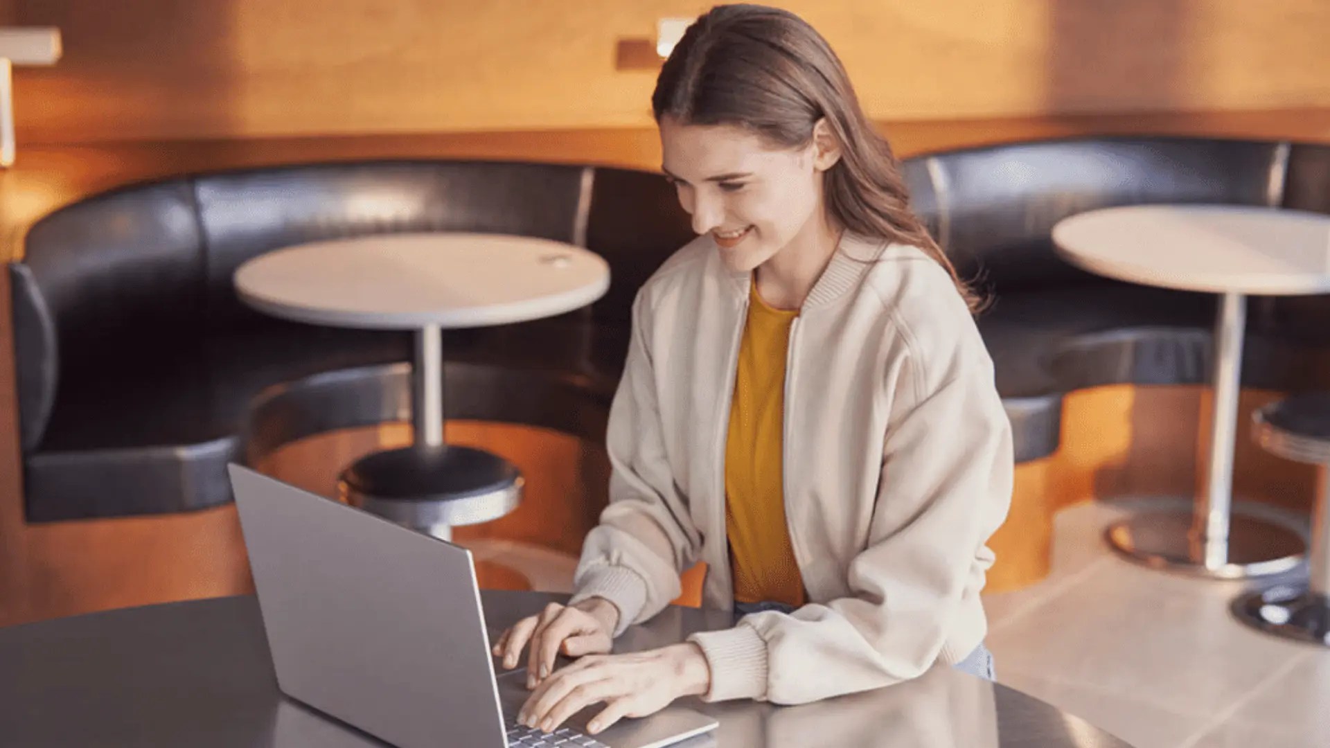Smiling woman using a silver new-generation AI laptop powered by Microsoft Copilot at a cafe table.